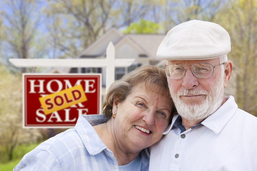 Smiling senior couple in front of a home sold sign